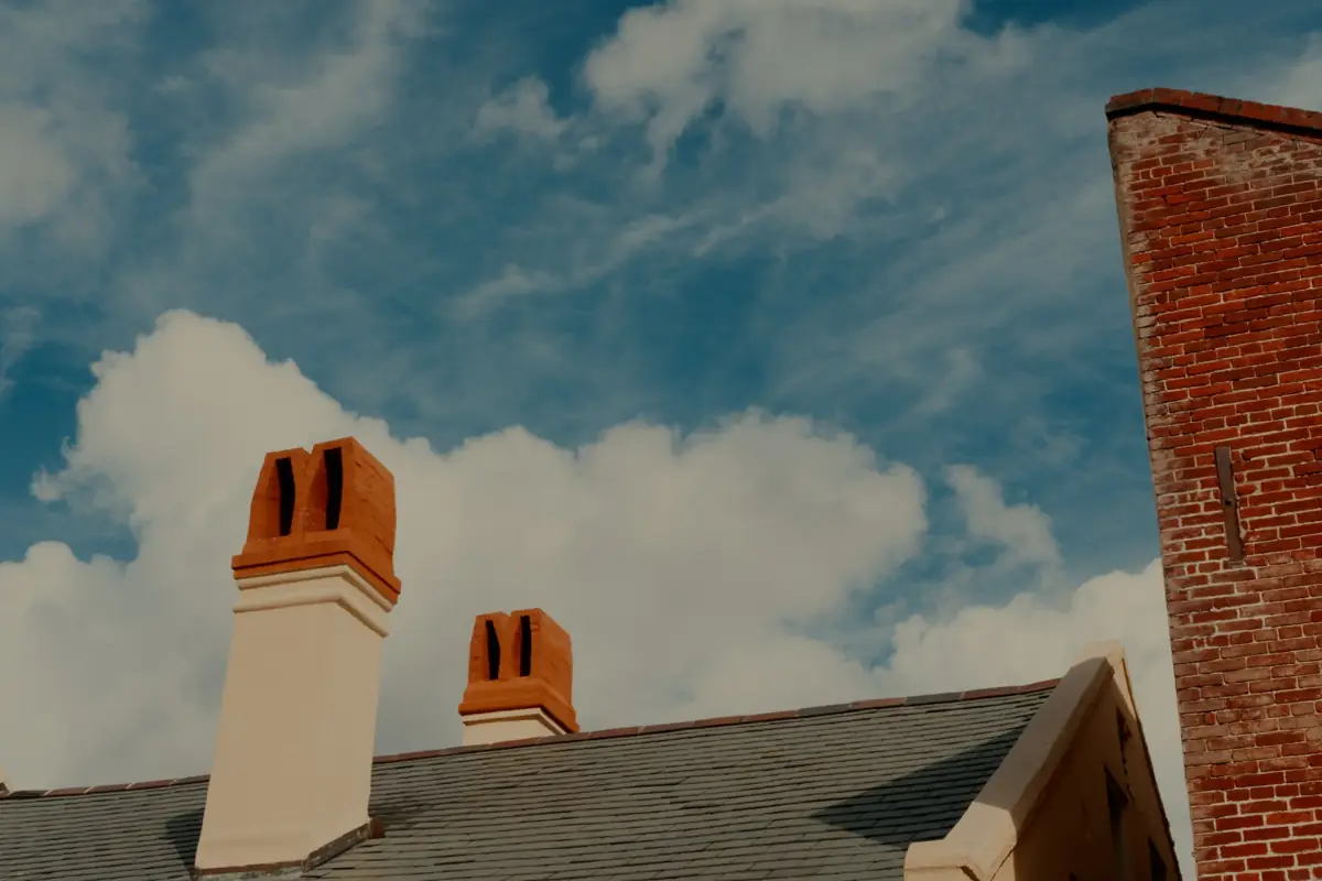 Two chimney tops with clay pots on a slate roof under a cloudy blue sky
