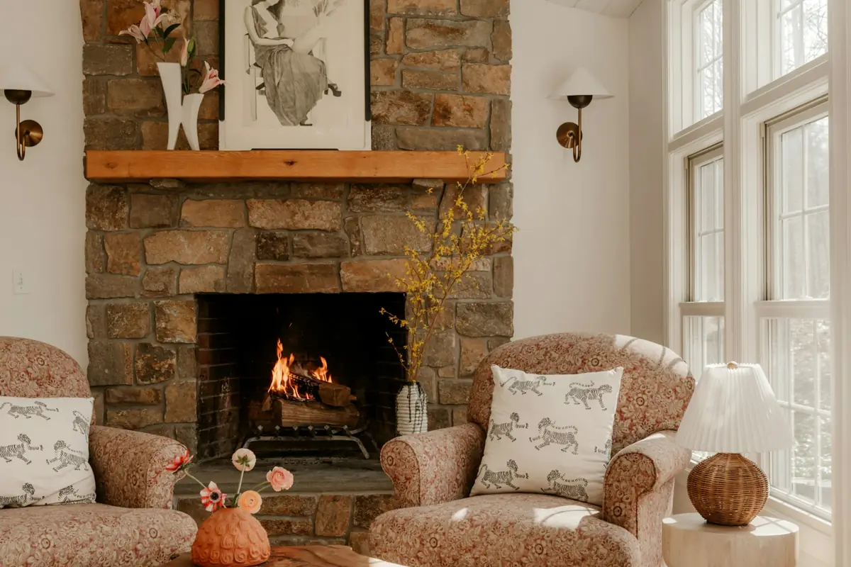 A living room with a stone fireplace, a wood mantel and two armchairs